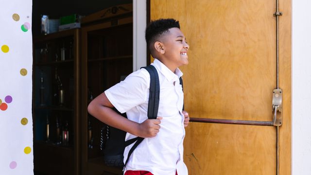 Un garçon souriant, cartable au dos, entre dans son école.