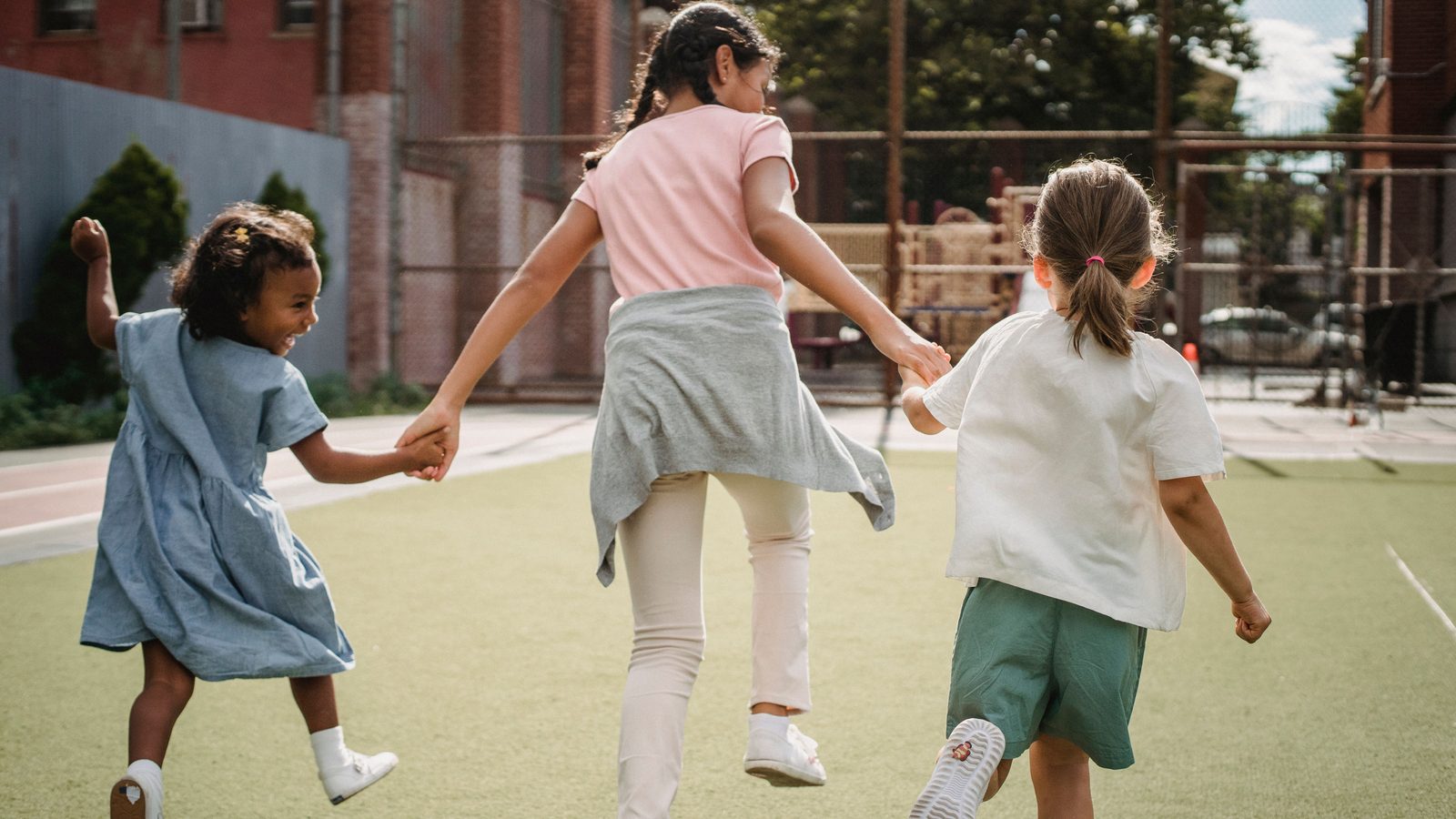 Trois enfants d'origines différentes courent main dans la main en plein air.
