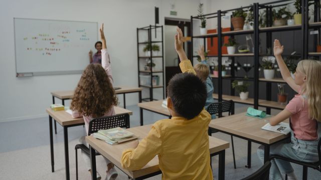 Des élèves lèvent la main dans une salle de classe animée.