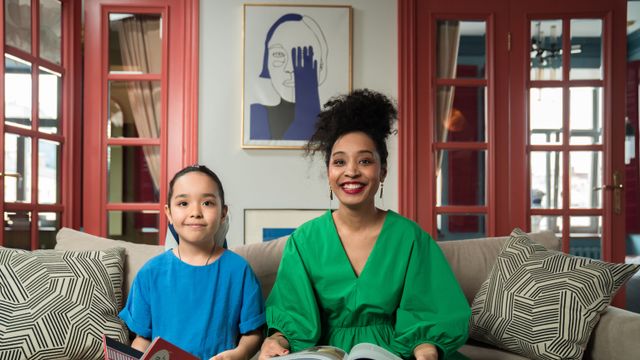 Une mère et sa fille lisent un livre ensemble, en souriant, dans un salon lumineux.