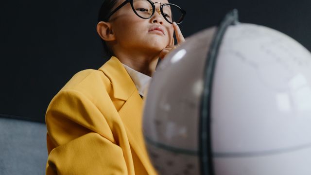 Un enfant en manteau jaune observe un globe terrestre, l'air songeur.